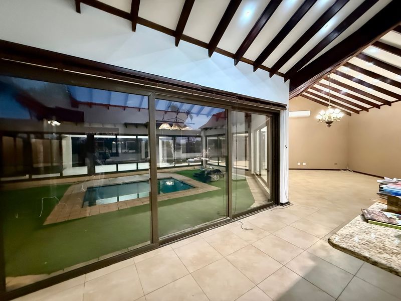 Spacious open-plan living area featuring exposed timber beams, tiled flooring, and large sliding glass doors providing a view of the pool area.