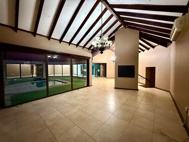 Spacious living area featuring high vaulted ceilings with exposed timber beams, tiled flooring, a built-in fireplace, and large sliding doors overlooking the pool area.