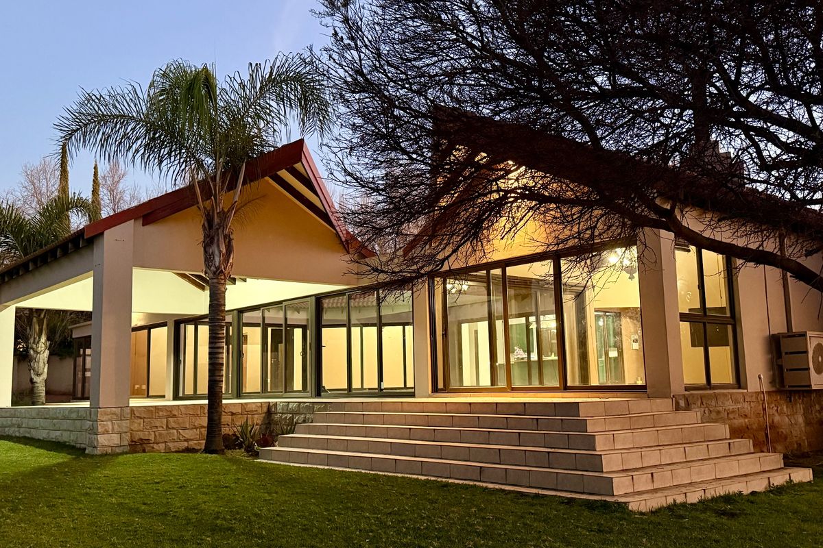 Rear view of the property featuring a spacious tiled patio, large sliding glass doors, and stone-clad steps leading to a well-maintained garden.