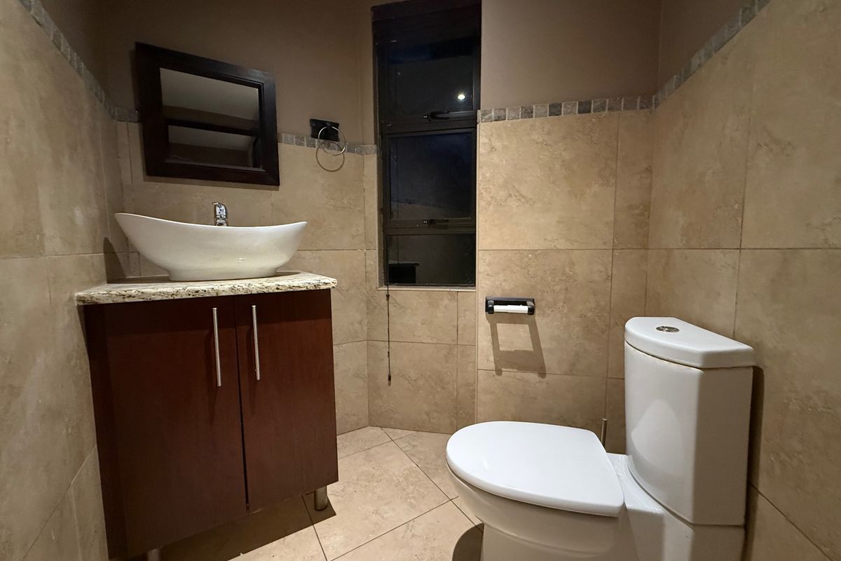 A compact bathroom featuring a modern vessel sink on a granite-topped vanity cabinet, tiled walls, and a standard toilet.