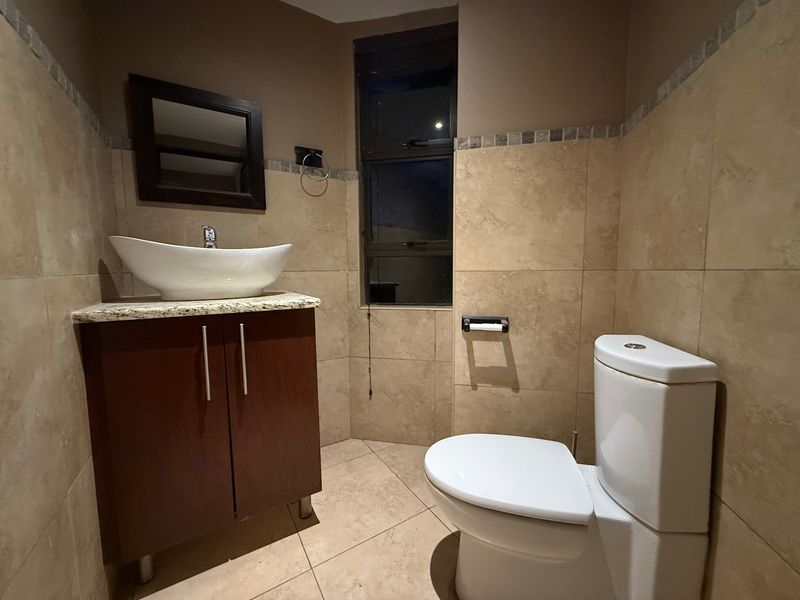 A compact bathroom featuring a modern vessel sink on a granite-topped vanity cabinet, tiled walls, and a standard toilet.