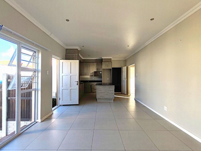 An open-plan living and kitchen area featuring neutral tiled flooring, modern cabinetry, and direct access to the exterior through glass doors.