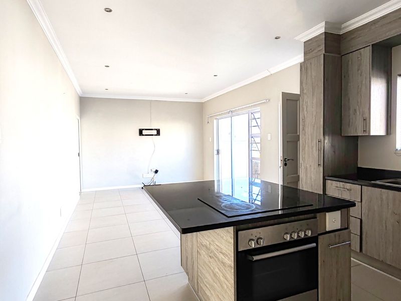 Spacious open-plan kitchen and living area featuring a central island with built-in oven, modern cabinetry, and neutral tiled flooring throughout.