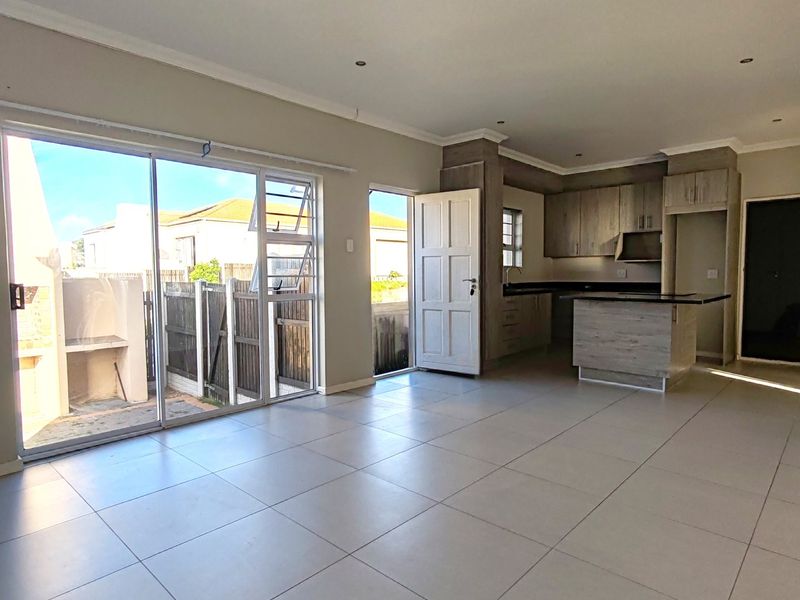 Spacious open-plan living and kitchen area featuring modern tiled floors, recessed lighting, and direct access to a private patio with a built-in braai.