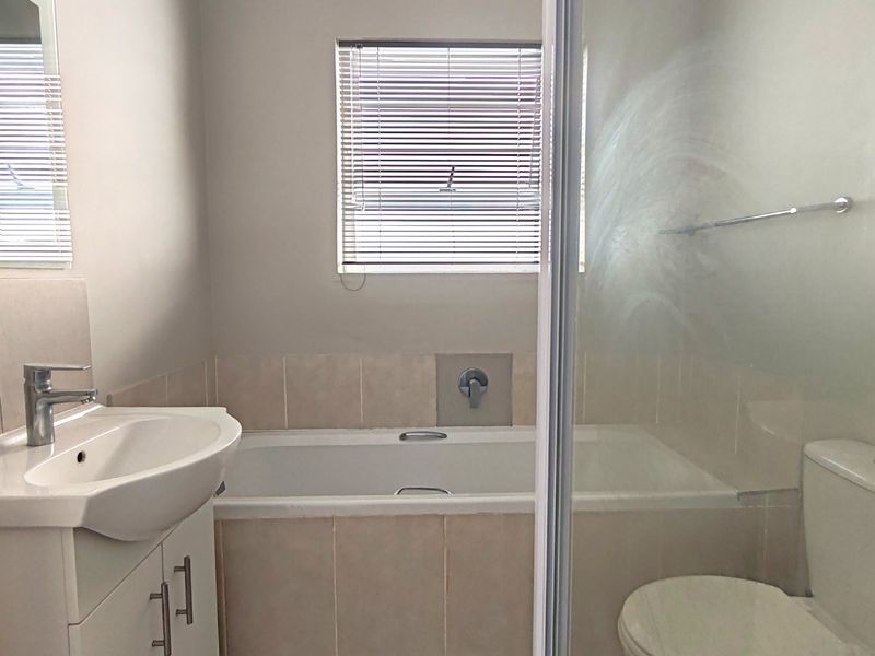 A clean, functional bathroom featuring a built-in bathtub, vanity with basin, toilet, and a glass-enclosed shower area with neutral tiling.