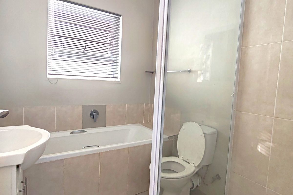 A functional bathroom featuring a built-in bathtub, a separate glass-enclosed shower, a pedestal basin, and a toilet with neutral wall and floor tiling.