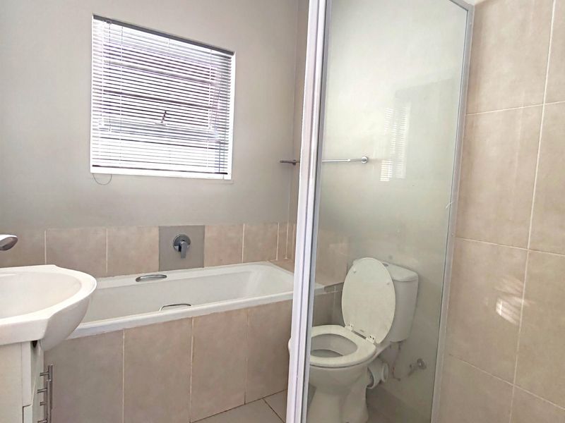 A functional bathroom featuring a built-in bathtub, a separate glass-enclosed shower, a pedestal basin, and a toilet with neutral wall and floor tiling.