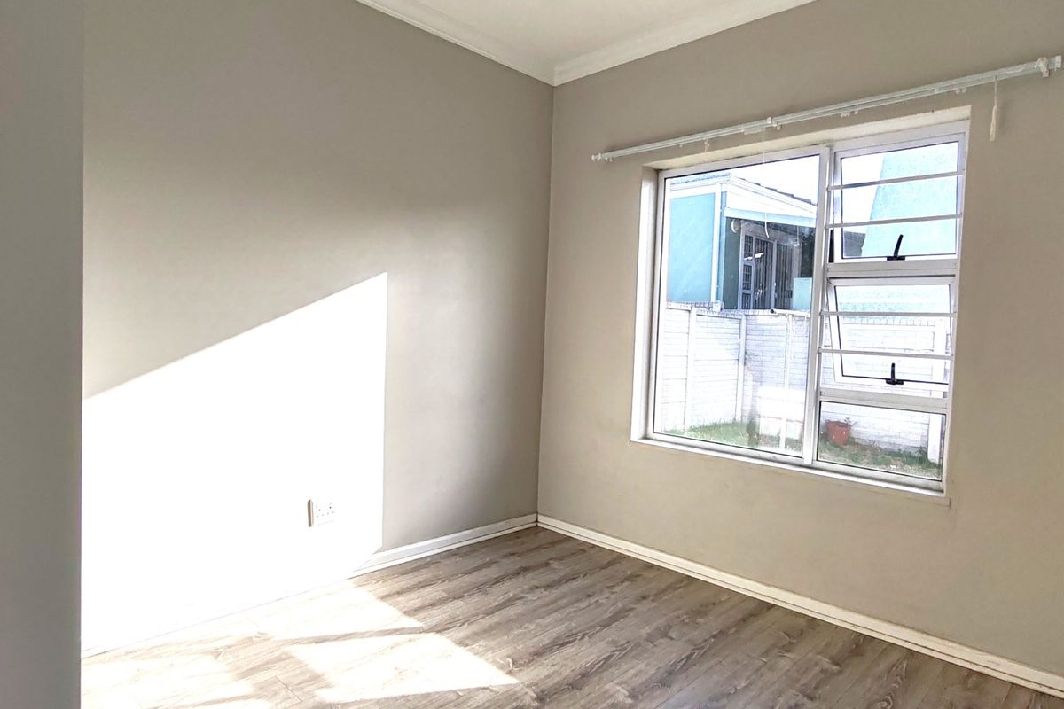 A bright, empty bedroom featuring modern laminate flooring, recessed downlighting, and neutral wall finishes, offering a clean and versatile space.