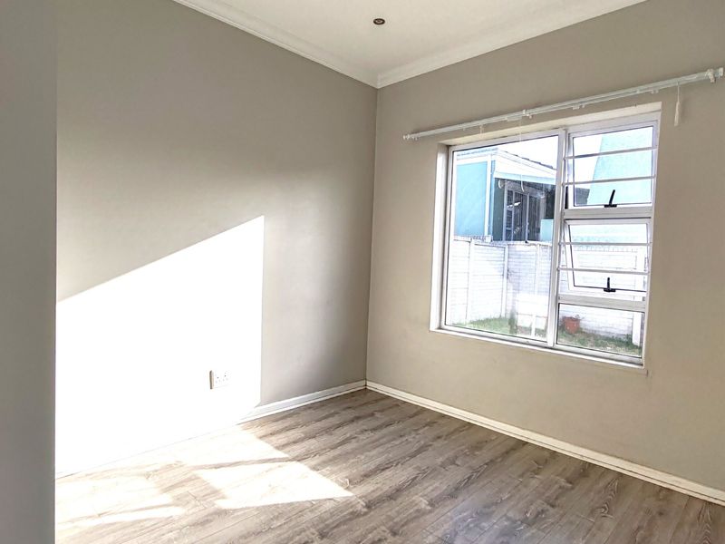 A bright, empty bedroom featuring modern laminate flooring, recessed downlighting, and neutral wall finishes, offering a clean and versatile space.