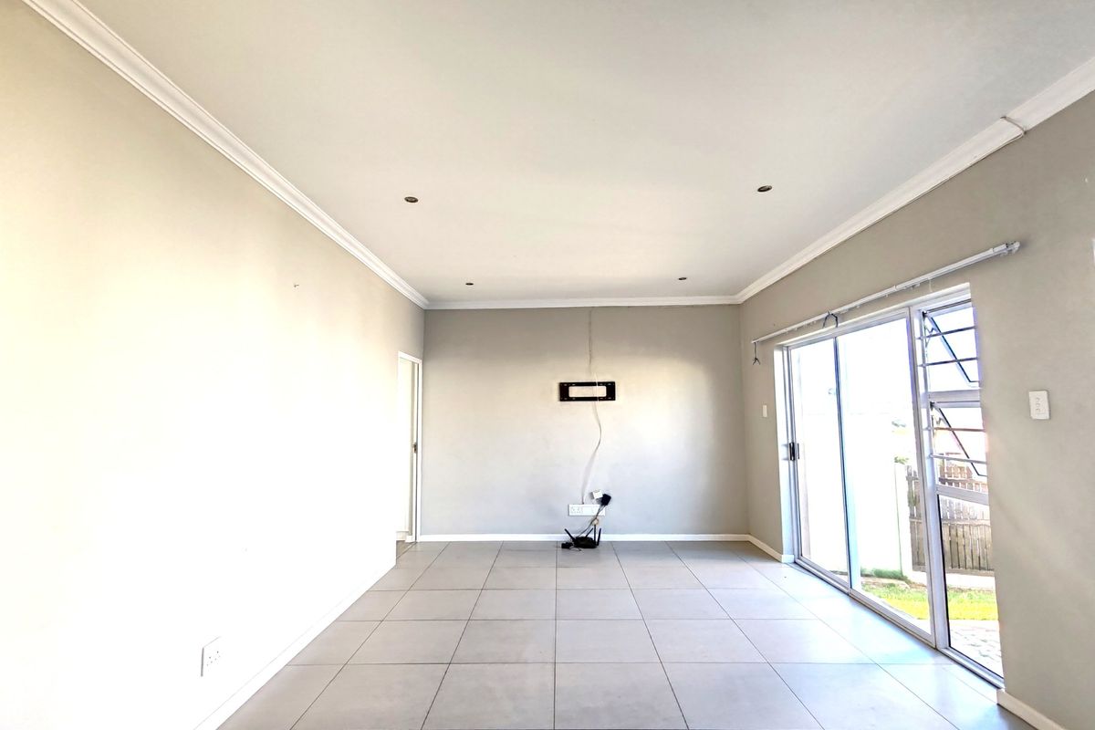 A bright, empty living room featuring neutral tiled flooring, recessed ceiling lighting, and a large sliding glass door providing access to the exterior.