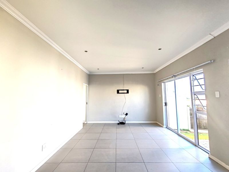 A bright, empty living room featuring neutral tiled flooring, recessed ceiling lighting, and a large sliding glass door providing access to the exterior.