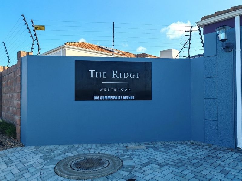 The entrance facade of The Ridge complex at 166 Summerville Avenue, featuring a blue boundary wall, paved driveway, and security electric fencing.