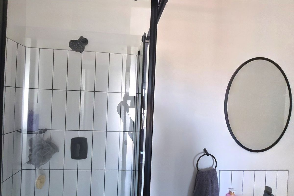 Modern bathroom featuring a walk-in shower with black-framed glass enclosure, subway wall tiling, and a contemporary oval wall mirror.