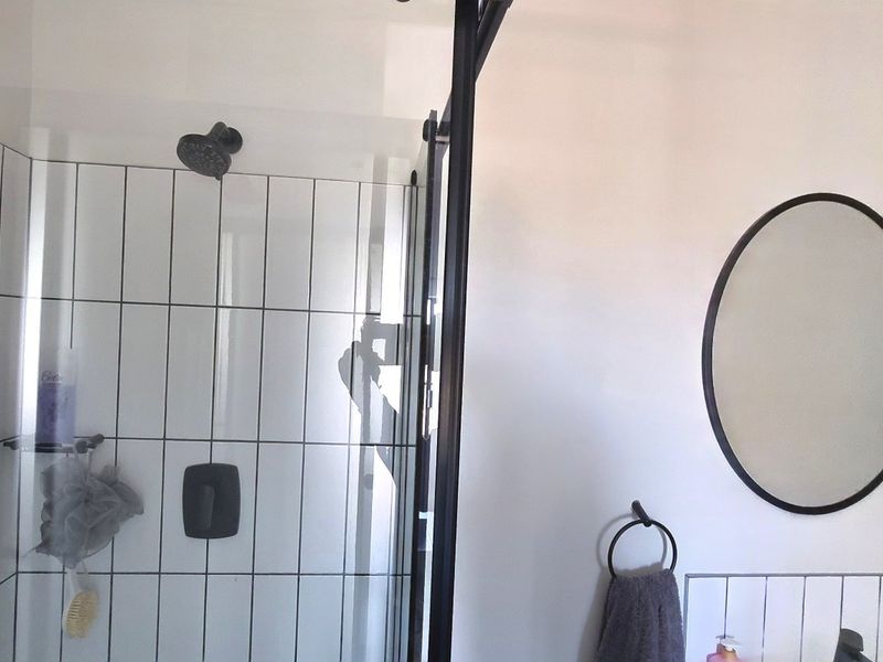Modern bathroom featuring a walk-in shower with black-framed glass enclosure, subway wall tiling, and a contemporary oval wall mirror.