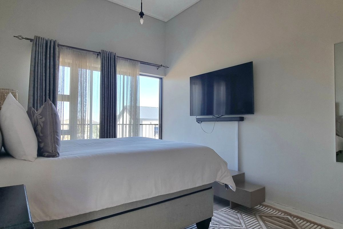A well-lit bedroom featuring a large sliding glass door with curtain tracks and a wall-mounted television setup.