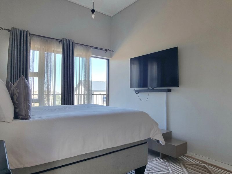 A well-lit bedroom featuring a large sliding glass door with curtain tracks and a wall-mounted television setup.