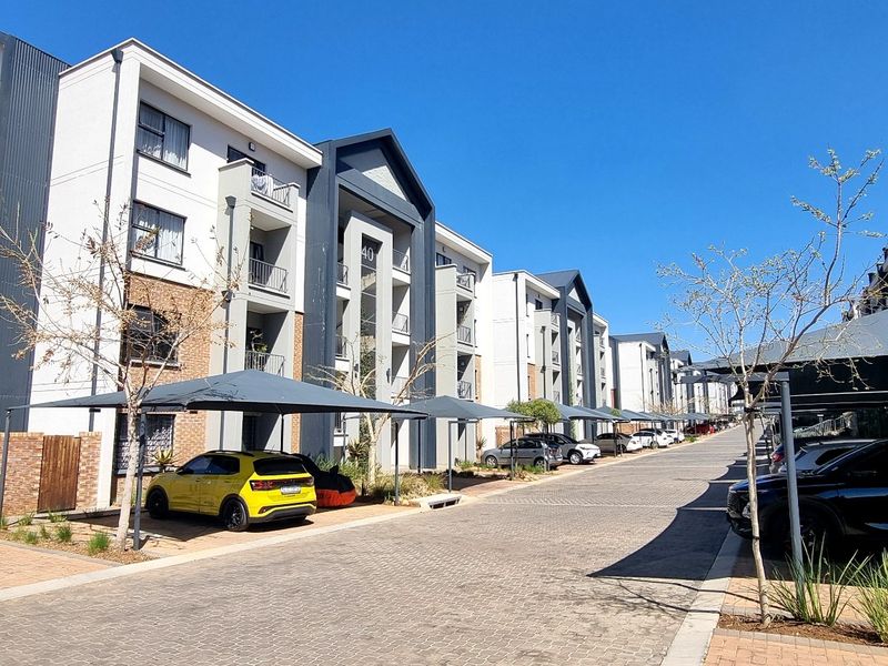 Exterior view of a modern multi-story apartment complex featuring paved driveways and covered parking bays.