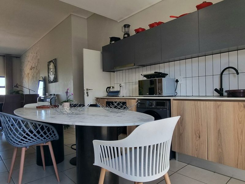 Modern open-plan living area featuring a contemporary kitchen with sleek cabinetry, integrated appliances, and tiled flooring, flowing into a bright lounge space.