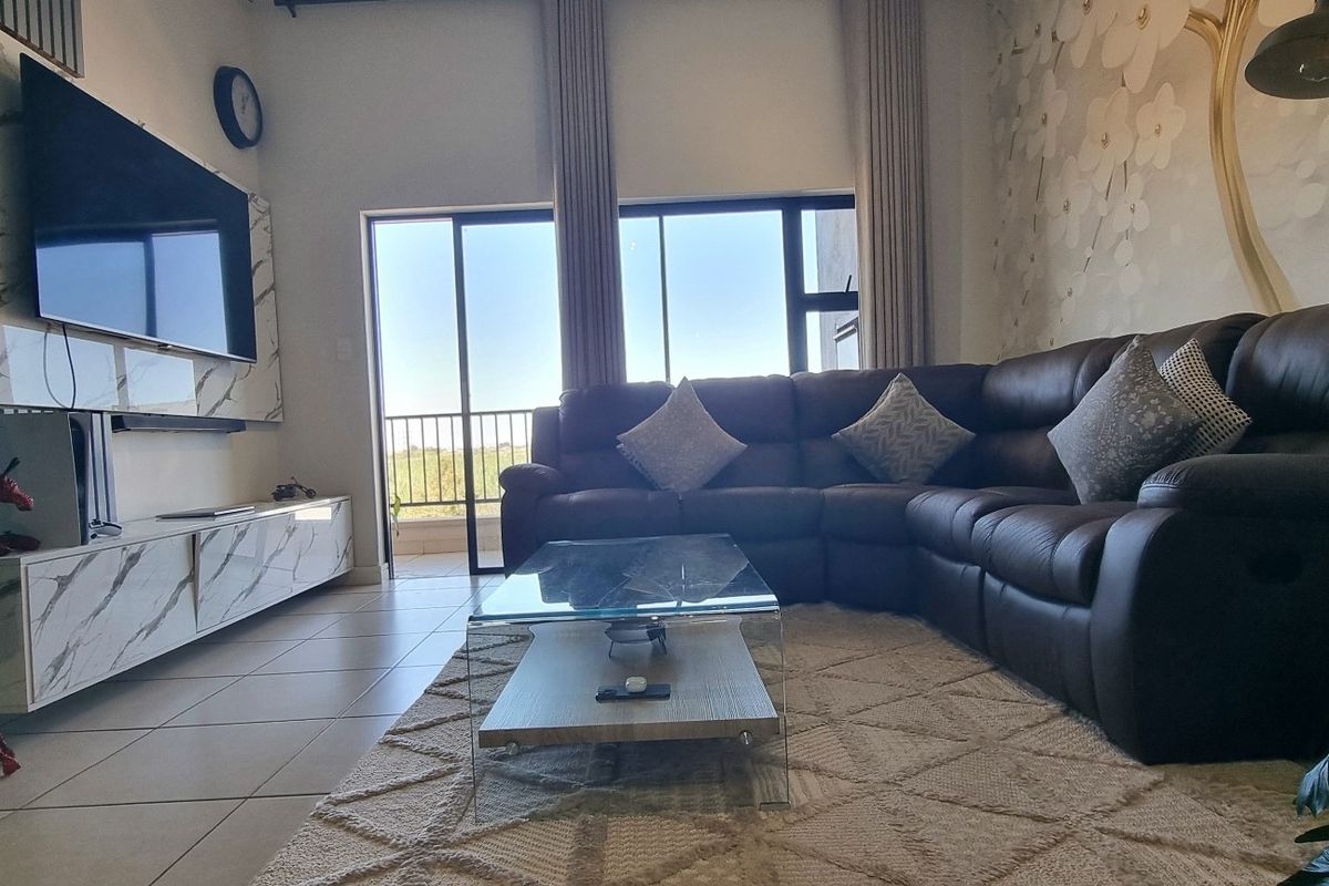 A well-maintained living room featuring tiled flooring, a modern built-in media console with marble-effect finishes, and a large sliding door leading to a balcony.