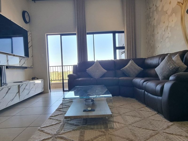 A well-maintained living room featuring tiled flooring, a modern built-in media console with marble-effect finishes, and a large sliding door leading to a balcony.