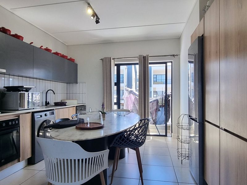 Modern open-plan kitchen featuring sleek cabinetry, built-in oven, tiled backsplash, and direct access to a balcony through sliding glass doors.