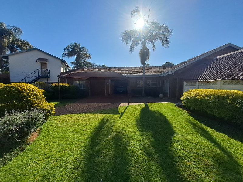 Front view of the property featuring a brick driveway, carport, and well-maintained lawn under a clear sky.