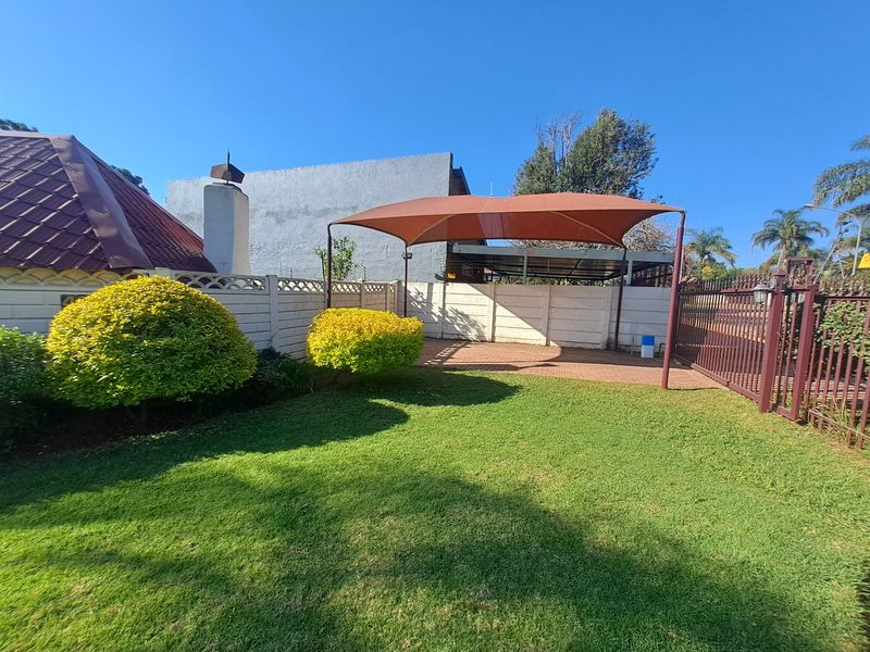 A well-maintained front garden area featuring a paved driveway, a shade sail structure, and secure perimeter walling with a metal gate.