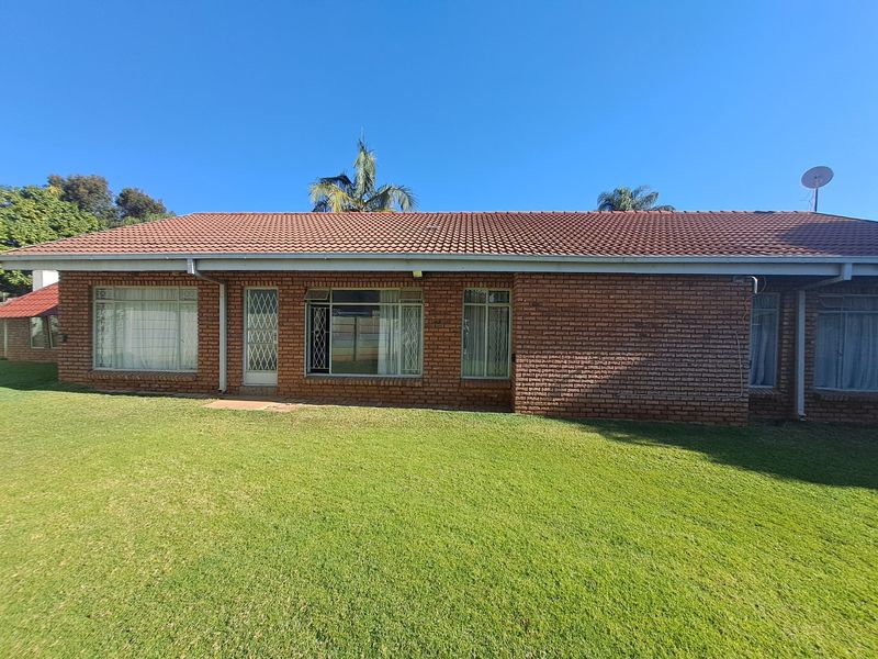 Rear view of a single-story face brick house featuring a tiled roof, large windows with security bars, and a well-maintained lawn.