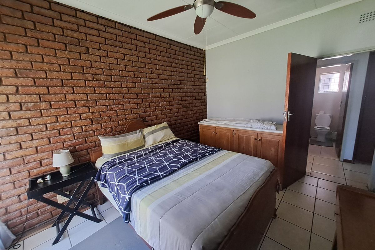 Bedroom featuring an exposed brick wall, tiled flooring, ceiling fan, and direct access to an en-suite bathroom with built-in storage.