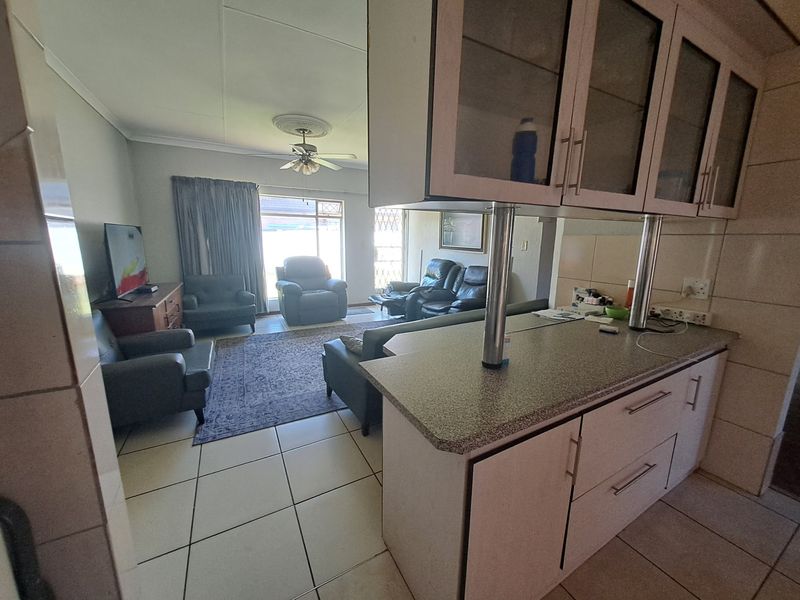 Open-plan living area featuring tiled flooring, a breakfast bar with built-in cabinetry, and a ceiling fan, leading to a sliding glass door.