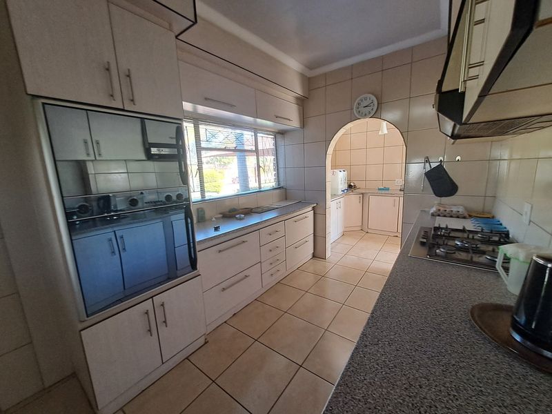 A functional kitchen featuring built-in cabinetry, stone countertops, a gas hob, and an integrated oven, with an adjoining scullery area through an arched doorway.