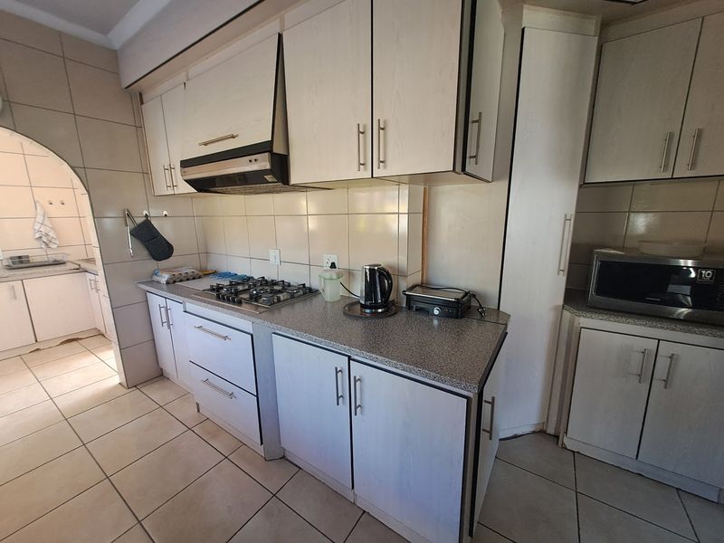 A functional kitchen featuring built-in cabinetry, a gas cooktop with extractor fan, tiled backsplash, and durable tiled flooring with an adjacent scullery area.