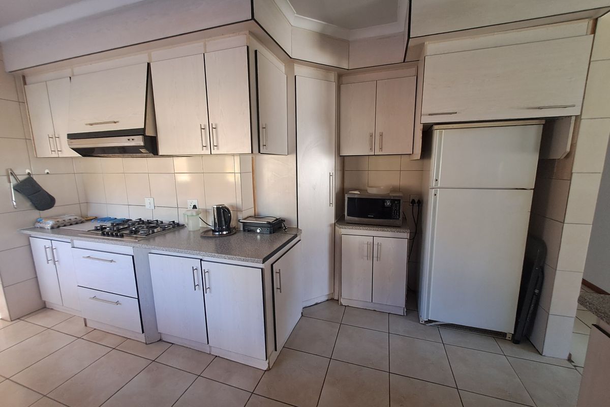 A functional kitchen featuring light-toned built-in cabinetry, a gas hob with extractor fan, tiled backsplash, and tiled flooring throughout.