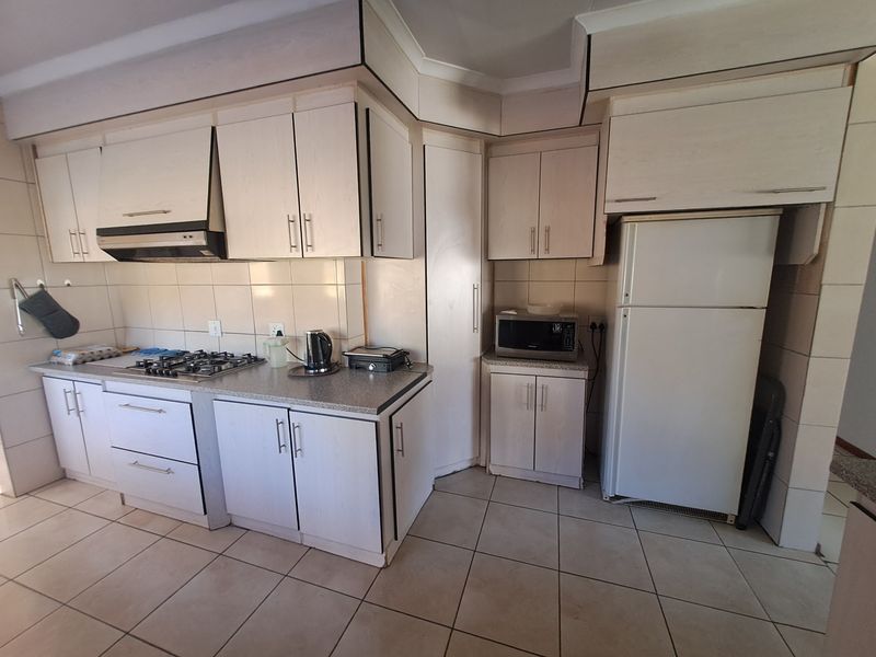 A functional kitchen featuring light-toned built-in cabinetry, a gas hob with extractor fan, tiled backsplash, and tiled flooring throughout.
