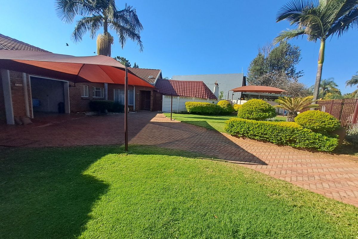 A well-maintained rear exterior featuring brick paving, a shade sail, and a landscaped garden with mature palm trees.