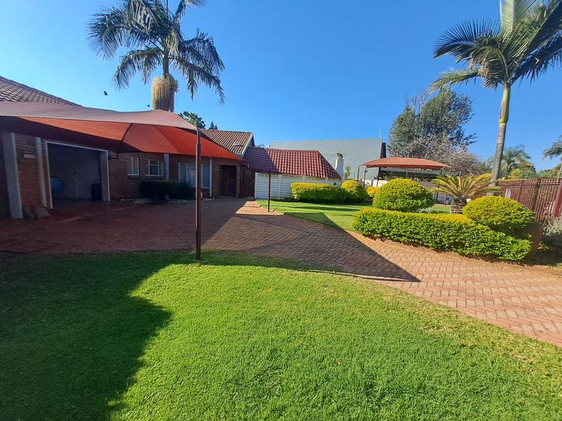 A well-maintained rear exterior featuring brick paving, a shade sail, and a landscaped garden with mature palm trees.