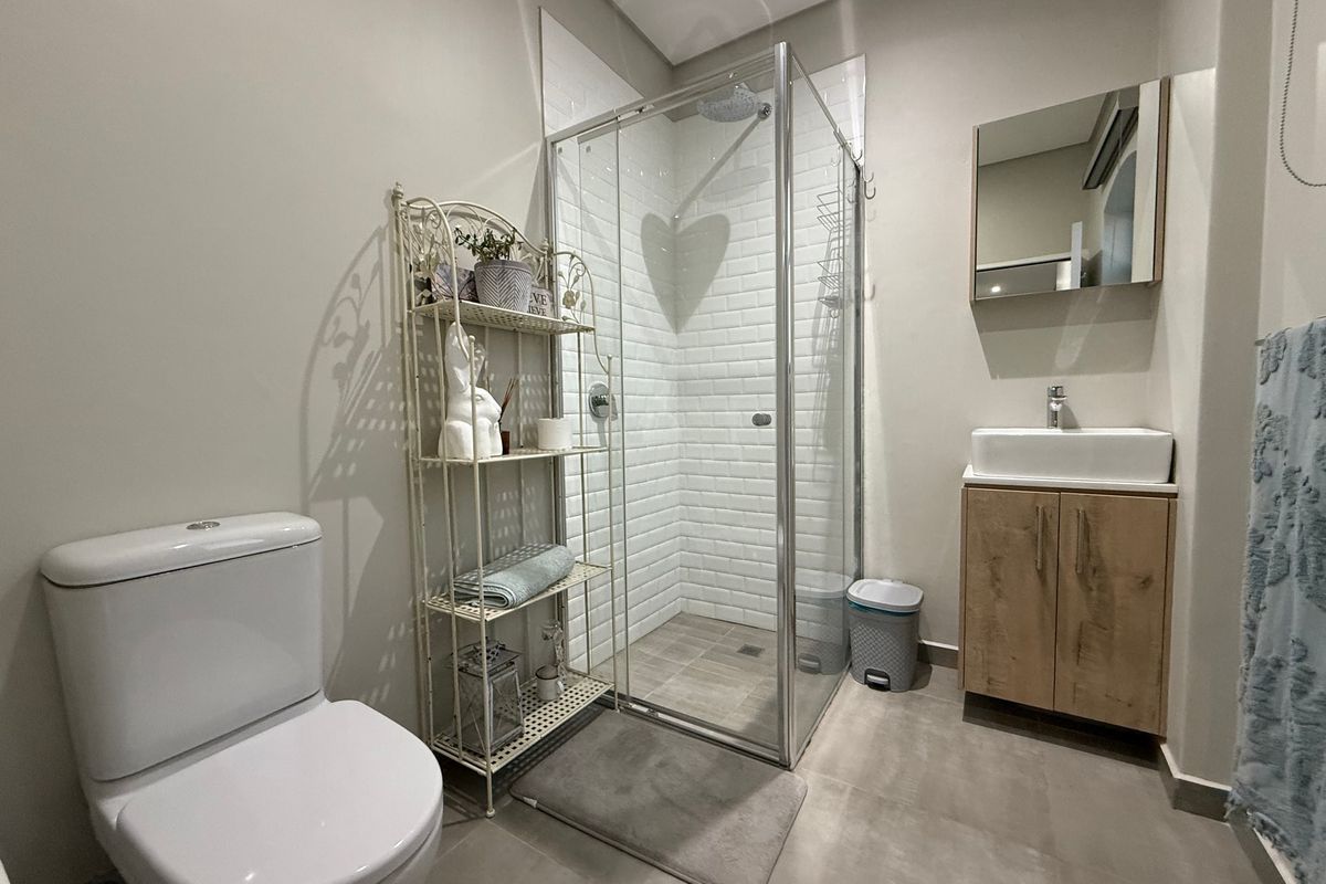 Modern bathroom featuring a glass-enclosed shower with subway tiling, a wood-finish vanity cabinet with a vessel sink, and a contemporary toilet.