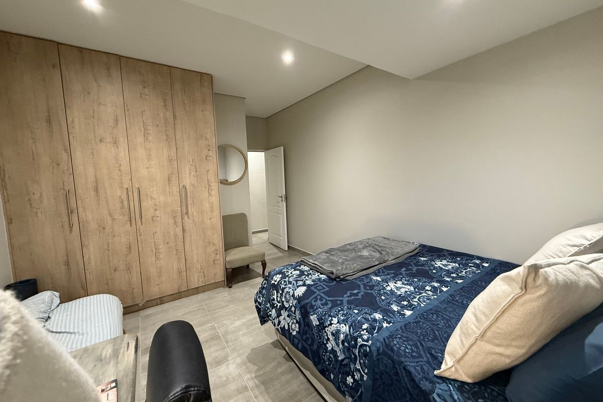 A well-maintained bedroom featuring modern wood-finish built-in wardrobes, neutral wall tones, recessed ceiling lighting, and durable tiled flooring.