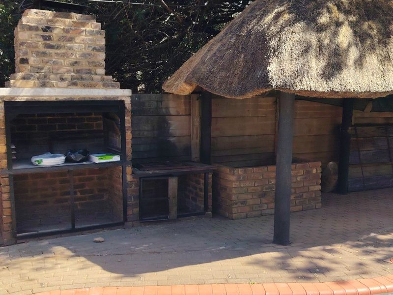 Outdoor entertainment area featuring a built-in brick braai and a thatched lapa structure, adjacent to the swimming pool.