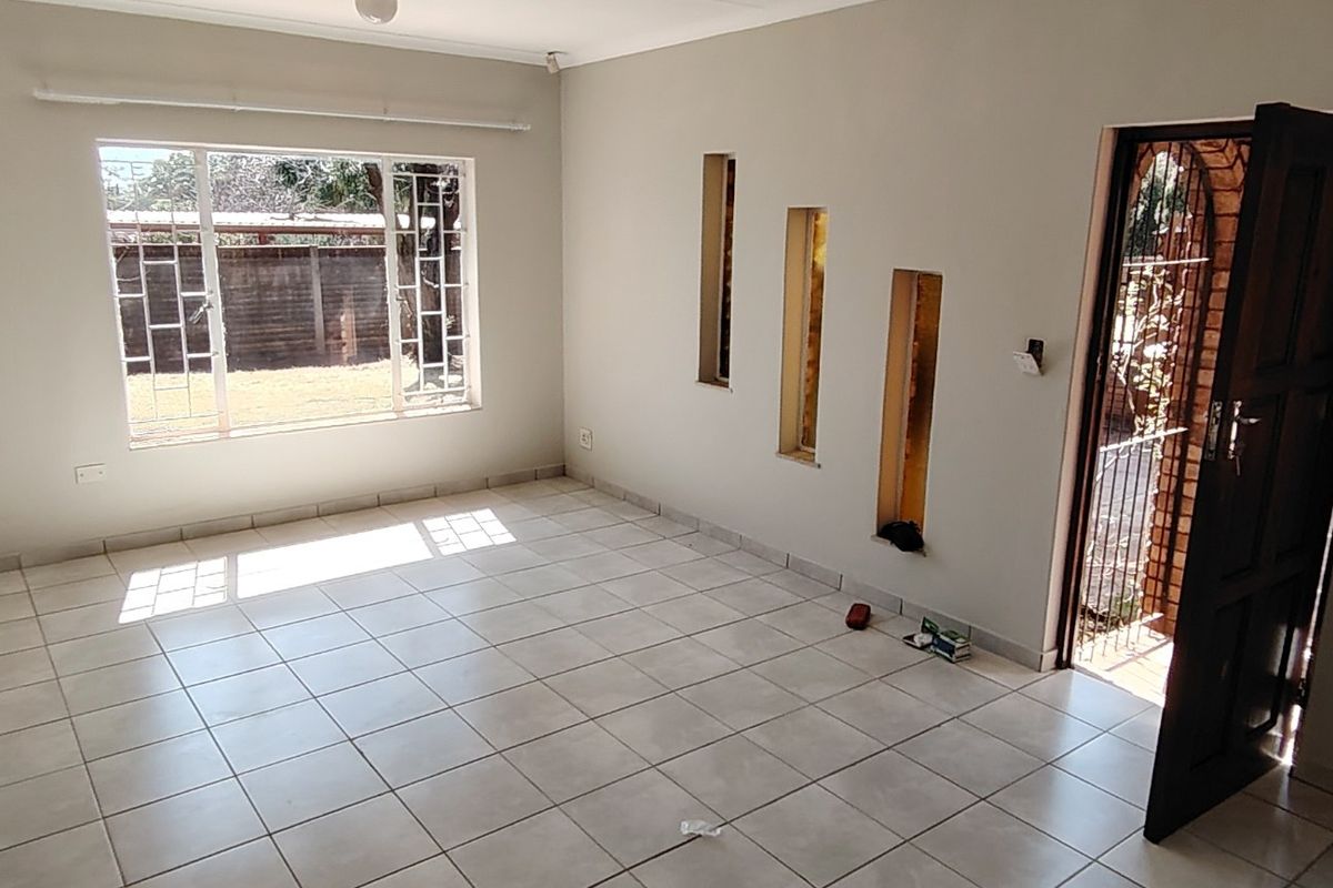 A bright, empty living room featuring neutral tiled flooring, security bars on windows, and unique recessed wall niches, providing a clean canvas for interior design.