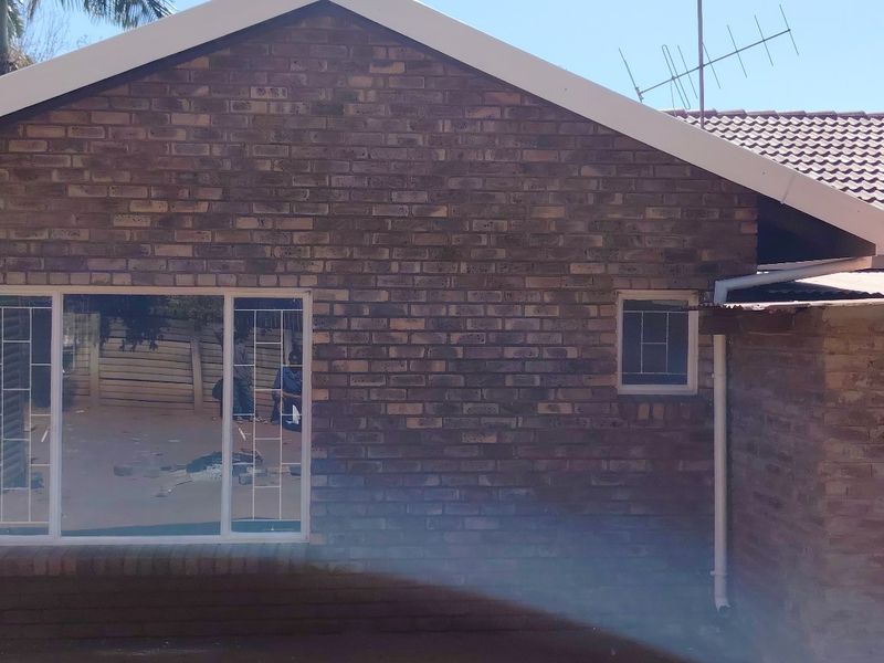 Rear exterior view of a face brick house featuring tiled roofing, aluminium window frames with security bars, and functional guttering systems.