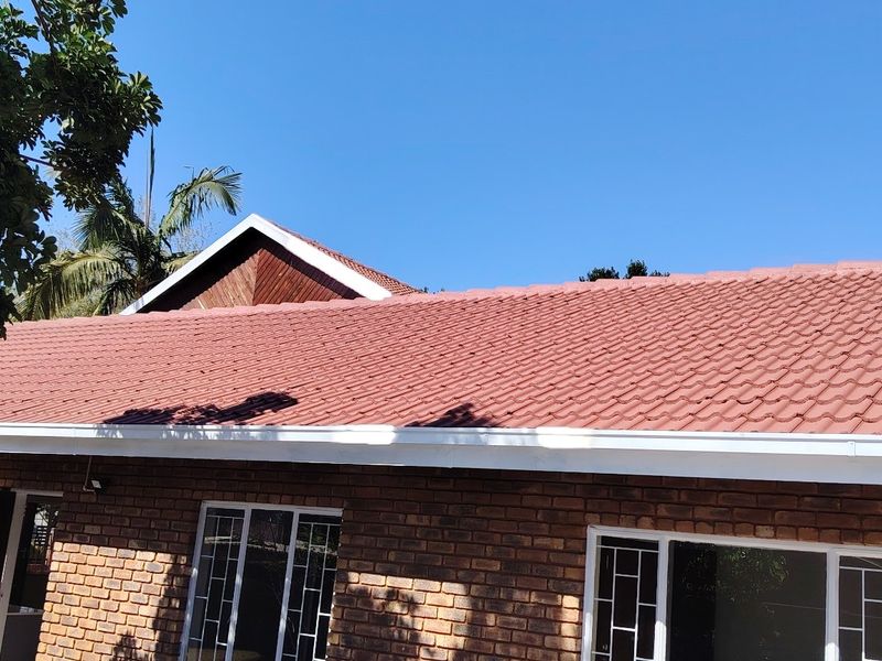 A view of the rear exterior featuring a well-maintained tiled roof, facebrick walls, and white aluminium window frames.