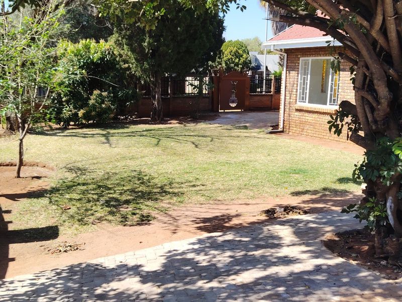 A view of the rear garden featuring a brick exterior wall, paved walkway, and established trees with a lawn area.