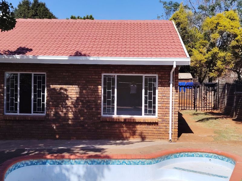 Rear view of a face brick house featuring a tiled roof, security-barred windows, and an integrated swimming pool with paved surround.