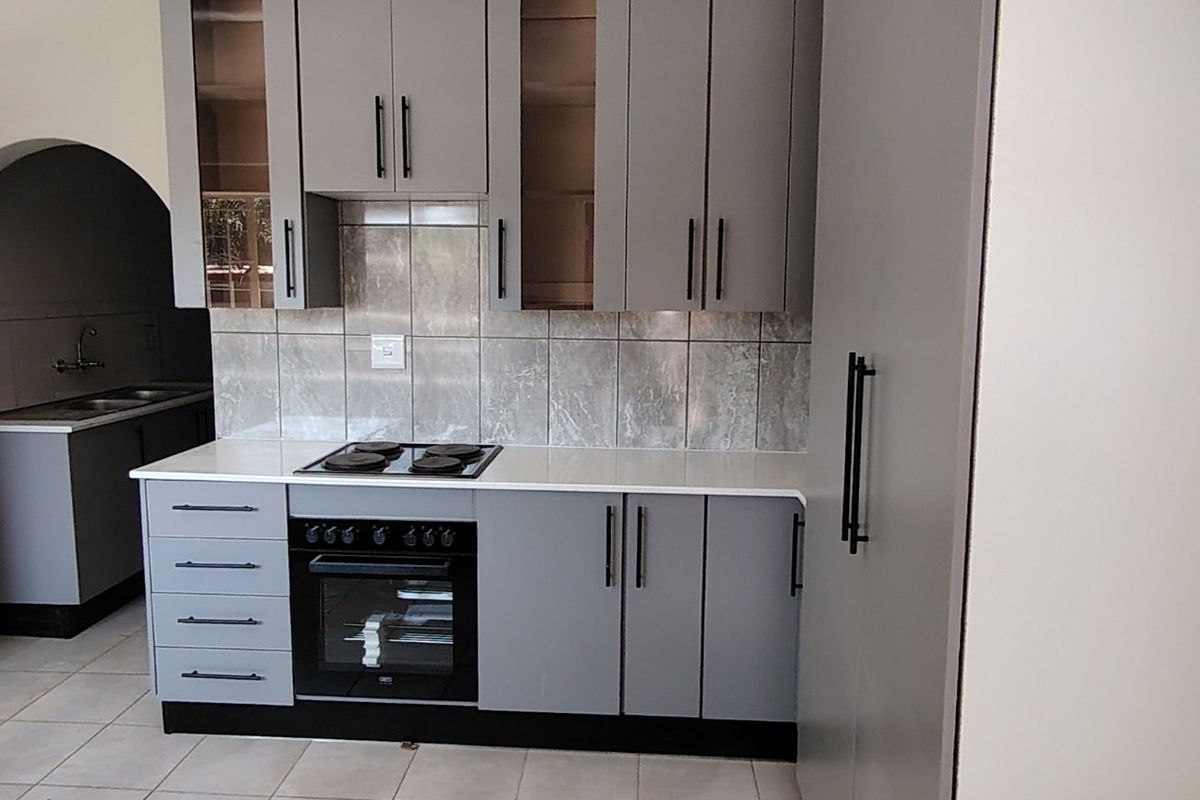 Modern kitchen featuring grey cabinetry, stone countertops, built-in oven and hob, tiled backsplash, and an adjacent scullery area with a double sink.