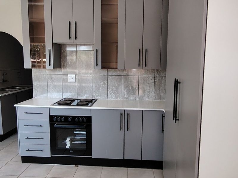 Modern kitchen featuring grey cabinetry, stone countertops, built-in oven and hob, tiled backsplash, and an adjacent scullery area with a double sink.