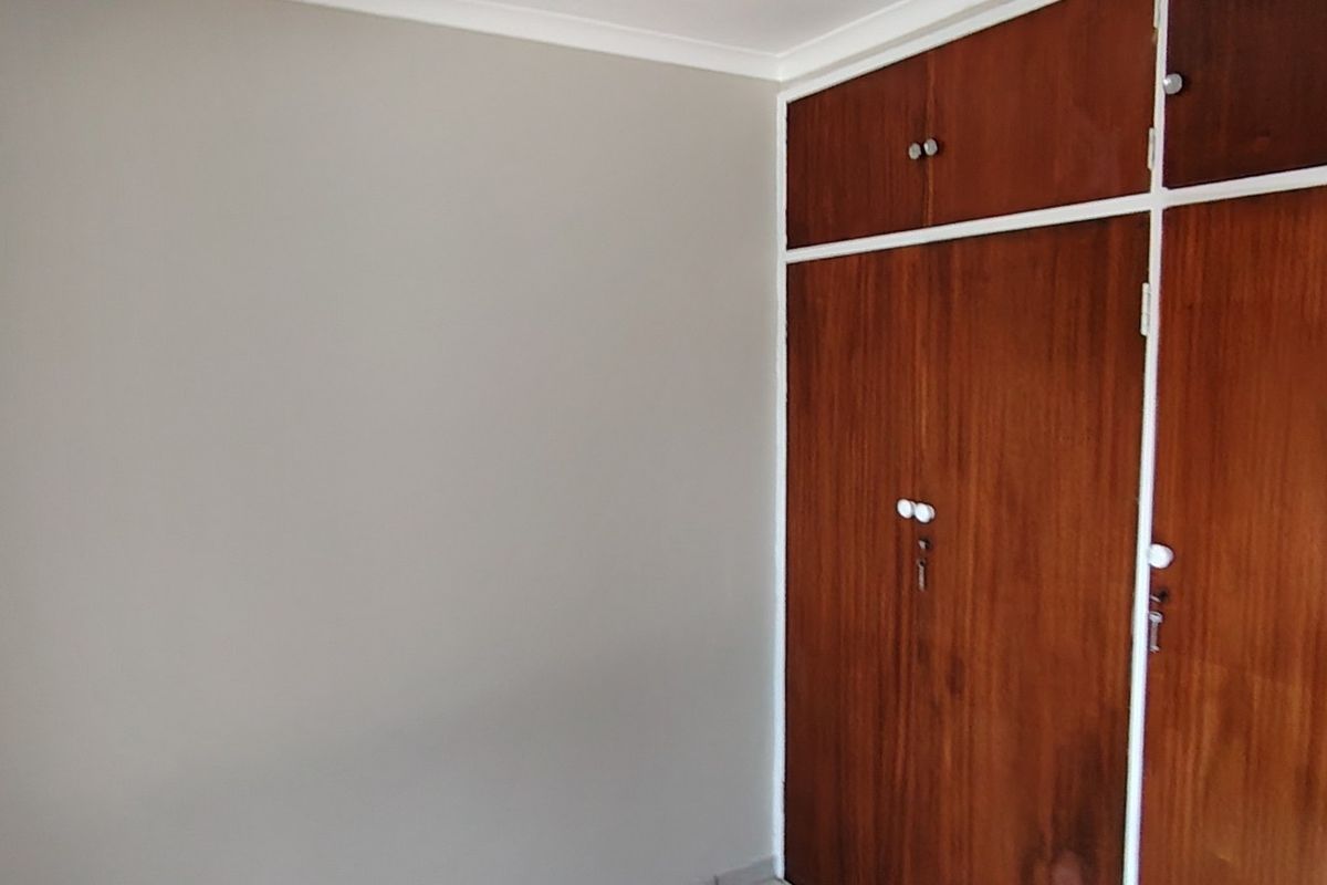 A clean, empty bedroom featuring neutral wall paint and classic built-in wooden cupboards with overhead storage compartments.