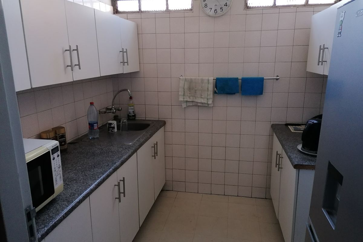 A functional galley-style kitchen featuring white cabinetry, granite-look laminate countertops, a stainless steel sink, and tiled wall finishes.