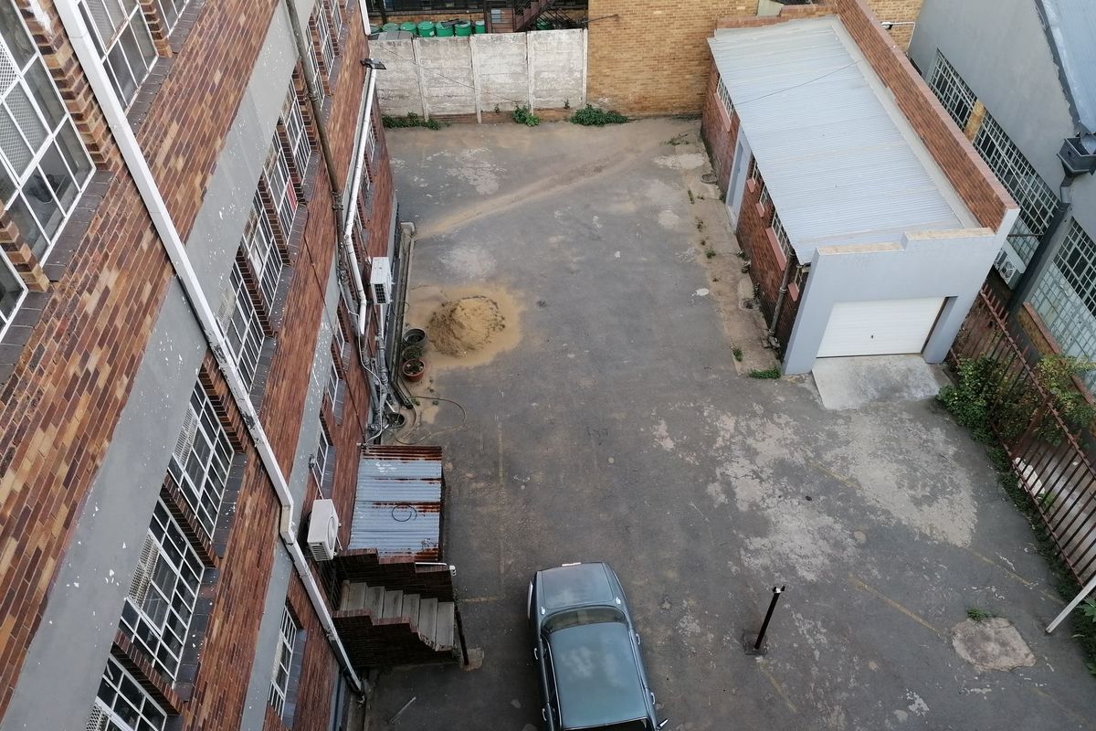 Aerial view of a commercial rear yard featuring brick building facades, an asphalt parking area, and a detached single garage structure.
