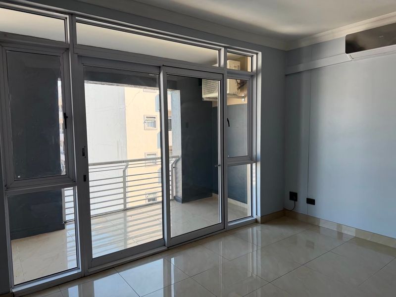 Bright and spacious living area featuring large sliding glass doors leading to a private balcony, tiled flooring, and a wall-mounted air conditioning unit.